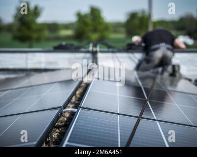Male team engineers installing stand-alone solar photovoltaic panel system. Electricians mounting blue solar module on roof of modern house. Alternati Stock Photo