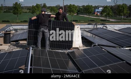 Male team engineers installing stand-alone solar photovoltaic panel system. Electricians mounting blue solar module on roof of modern house. Alternati Stock Photo
