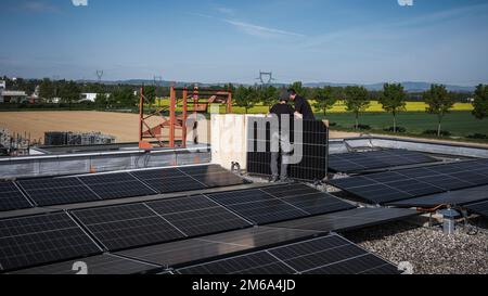 Male team engineers installing stand-alone solar photovoltaic panel system. Electricians mounting blue solar module on roof of modern house. Alternati Stock Photo