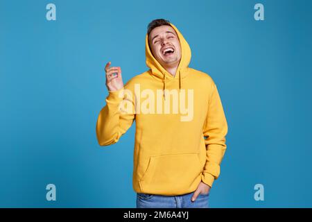 positive handsome man in yellow sweatshirt on blue Stock Photo