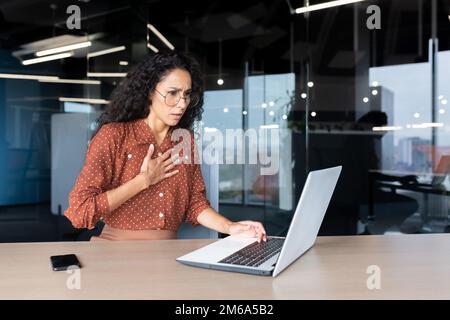 Anxious and scared business woman working inside office, Hispanic woman panic attack and breathing problem, female worker with laptop working. Stock Photo