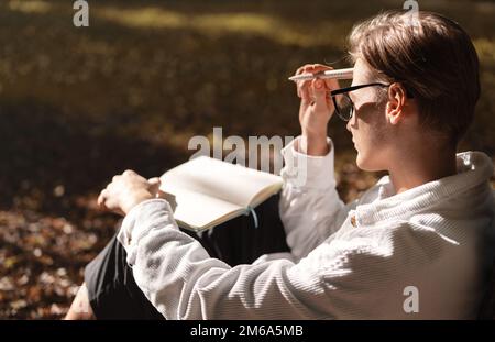 Woman sitting on ground in park with  diary on hir lap and thinking about notes in notebook. Stock Photo