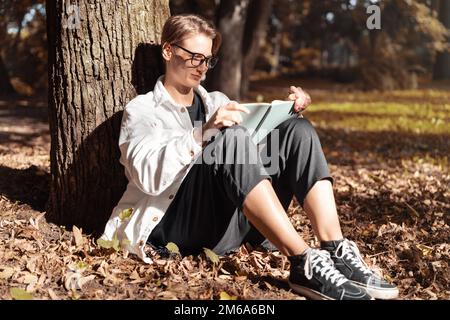 Young short hair woman sitting on ground in park and reading book. Stock Photo