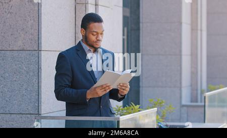 African American man ethnic businessman employer entrepreneur office worker standing on balcony holding day planner reading paper book read business Stock Photo