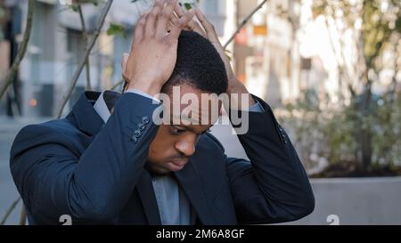 Stressed exhausted ethnic man male guy company employee having painful head pain headache stress with lost job fired unemployment in city. Tired Stock Photo