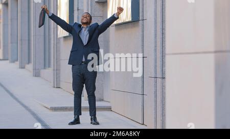 Overjoyed happy success African American man worker manager intern businessman winner walk outdoors feel overjoyed excited jumping dancing celebrating Stock Photo