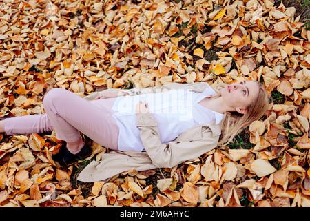 Woman in coat and white shirt lying on autumn leaves Stock Photo