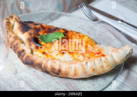 Calzone Pizza. Neapolitan pizza stuffed with cheese, tomato and other ingredients such as meat or vegetables. Authentic Italian recipe. Stock Photo