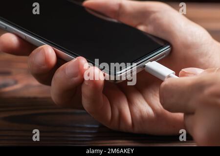 Man hands plugging a charger in a smart phone. Man using smartphone with powerbank. Man charging battery on mobile phone at home Stock Photo