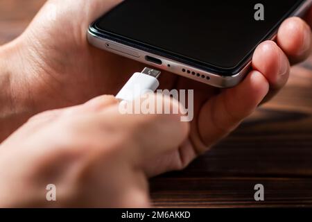 Man hands plugging a charger in a smart phone. Man using smartphone with powerbank. Man charging battery on mobile phone at home Stock Photo
