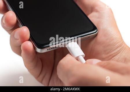 Man hands plugging a charger in a smart phone. Man using smartphone with powerbank. Man charging battery on mobile phone at home Stock Photo