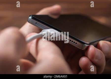 Man hands plugging a charger in a smart phone. Man using smartphone with powerbank. Man charging battery on mobile phone at home Stock Photo