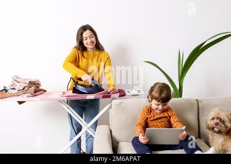 Mom is doing household chores while the child is studying online. Stock Photo