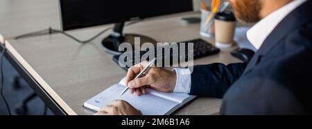 Close up of businessman sitting at desk, working online, using computer and taking notes at office, panorama, cropped Stock Photo