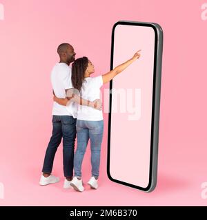 Rear back view of black spouses using big smartphone with blank screen, woman touching huge display panel, mock up Stock Photo