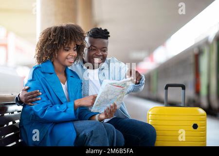 Black Couple Checking Travel Route On Map While Sitting At Railway Station Stock Photo