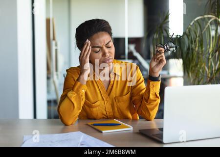 Unhappy black female freelancer feeling tired of working on laptop, suffering from headache in office interior Stock Photo
