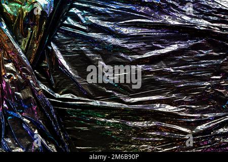 Black color plastic wrap background. Dark crumpled wrinkled plastic cellophane. Reflecting colorful iridescent light and shadow on creases and folds Stock Photo