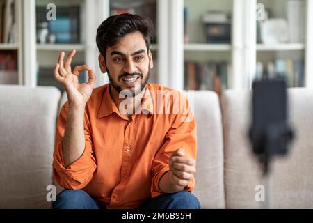 Positive handsome arab guy vlogger streaming from home, using phone Stock Photo