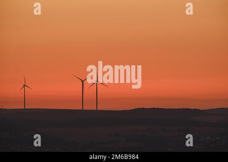 Three big windmill and wind wheel at a field in Germany near the city Würzburg at sunset. Stock Photo