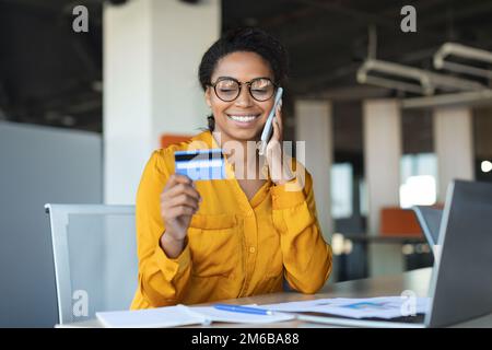 Online banking. Young african american businesswoman using smartphone and credit card, making money transfers Stock Photo