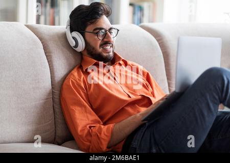 Relaxed arab man watching movile on laptop, home interior Stock Photo