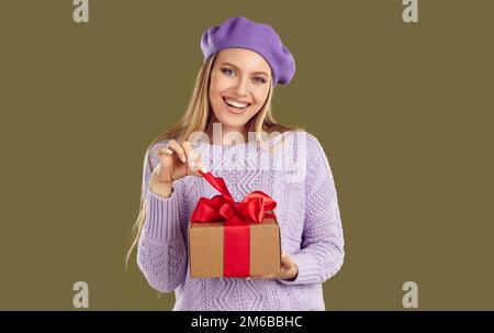 Beautiful and cute woman with joyful facial expression is untying ribbon on gift box. Stock Photo