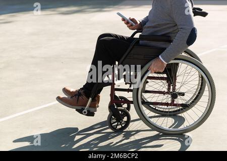 Man in wheelchair using a mobile phone outdoors. Stock Photo