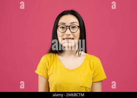 Portrait of positive chinese woman wearing glasses and looking to camera, posing over pink studio background Stock Photo