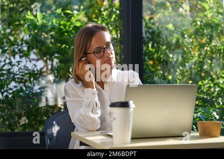 Young woman on video call using laptop. Happy businesswoman having a virtual meeting with a client in a cafe Stock Photo