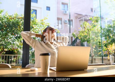 Exhausted businesswoman stretching with arms raised while working in coworking office. Stock Photo