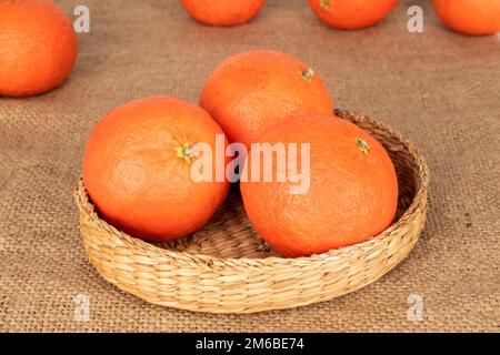 Three sweet juicy tangerines in a straw plate on a jute cloth, macro. Stock Photo