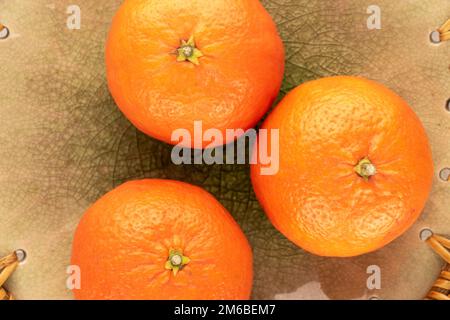 Three juicy tangerines on a ceramic dish, macro, top view. Stock Photo