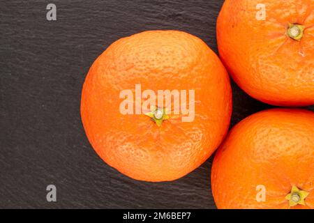 Three juicy tangerines on slate stone, macro, top view. Stock Photo