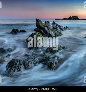 The rocks in the sea at sunset near the Long Strand, Ireland Stock Photo