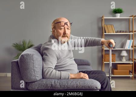 Senior man holding walking stick while sitting on sofa Stock Photo