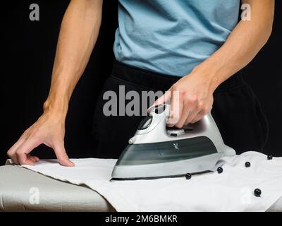 Male person using a steaming hot iron, on a white shirt Stock Photo