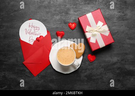 Card with text HAPPY VALENTINE'S DAY, cup of latte, cookie and gift on dark background Stock Photo