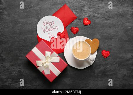 Card with text HAPPY VALENTINE'S DAY, cup of latte, cookie and gift on dark background Stock Photo