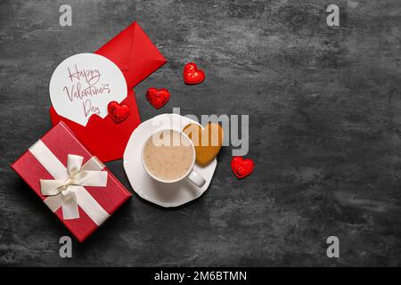 Card with text HAPPY VALENTINE'S DAY, cup of latte, cookie and gift on dark background Stock Photo