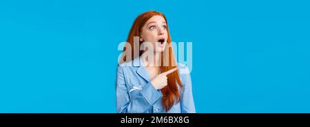 Omg check it out. Startled and emotional impressed redhead female drop jaw, staring upper left corner with amazed expression, popping eyes at incredib Stock Photo