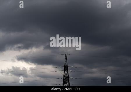 Electricity transmission pylon silhouetted against a cloudy sky. Stock Photo