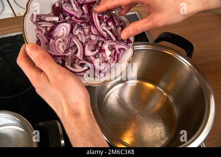 View on hands of a man roasting onions in a pot with coconut oil. Stock Photo