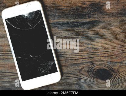 A close up of a damaged mobile phone with cracked screen for repair on a wooden background with copy space Stock Photo