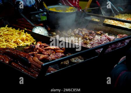 Romanian traditional food being cooked outdoor for sale at Christmas market in Bucharest in the evening. Pork meat, sausages, polenta and fries. Stock Photo