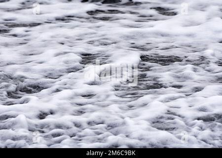 Natural sea water pattern. Foamy water runs out on a beach at wintertime. Small waves with whitecaps. Baltic Sea, Mecklenburg-Vorpommern, Germany Stock Photo