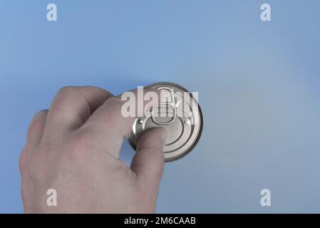 A man's hand opens a tin can. Blue background, close-up Stock Photo