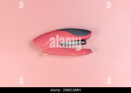 Red stapler on a pink background. Close-up Stock Photo