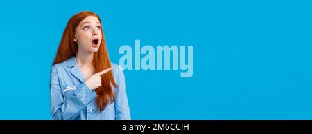 Omg check it out. Startled and emotional impressed redhead female drop jaw, staring upper left corner with amazed expression, popping eyes at incredib Stock Photo