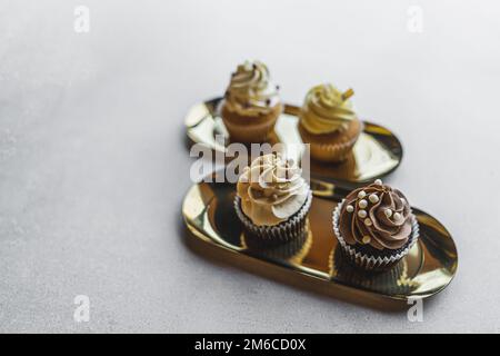Four cupcakes decorated with cream and pearls placed on two golden plates. Blurred background. High quality photo Stock Photo